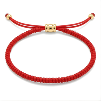 Jewelry: Bright red braided string bracelet with an adjustable design, featuring a central gold-toned barrel bead and two smaller gold beads securing the ends