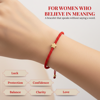 Product photograph of a woman's wrist wearing a red string bracelet with a gold star charm, on a light background displaying the headline 'FOR WOMEN WHO BELIEVE IN MEANING' and accompanying keywords Luck Protection Confidence Balance Clarity Love