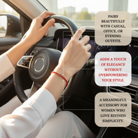 Photograph of a woman's hands on a dark car steering wheel, showcasing a vibrant red braided bracelet with a small gold star charm on her left wrist, set against a softly blurred urban background