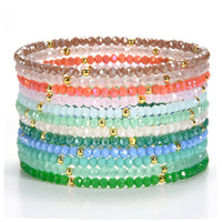 Beaded bracelets a vibrant stack of colorful faceted glass beads in a gradient from soft browns and corals to cool blues and greens, interspersed with tiny shiny gold spacer beads, on a white surface