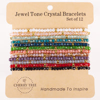Cherry Tree Collection Jewel Tone Crystal Bracelets a handmade set of twelve featuring faceted beads in colors like white pink teal red and black with gold accents displayed on a kraft paper backing with the slogan Handmade To Inspire