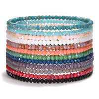 Product photography of stacked vibrant faceted glass bead bracelets showcasing a gradient of colors from teal, pink, and peach to orange, green, and deep purple on a white surface
