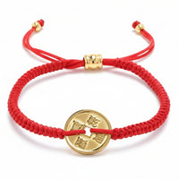 A red braided string bracelet featuring a gold-colored Chinese coin charm with a square hole and Qianlong Tongbao characters, secured with an adjustable sliding knot and gold beads