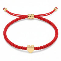 Red braided string bracelet featuring a central gold heart charm and an adjustable gold bead knot closure